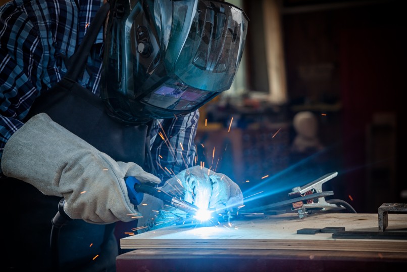 A welder clad in protective work attire diligently using a welding machine to fuse metal materials in an industrial workshop.