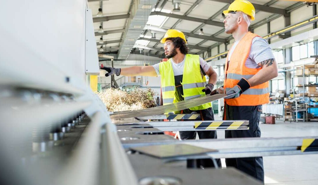 Male manual workers inspecting sheet metal for quality control in an industrial factory setting for manufacturing.